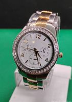 Front view of men's quartz watch, showing white dial with Arabic numerals, three subdials and rhinestone bezel, two-tone silver and gold metal band.