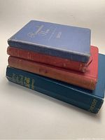 Four old hardcover books stacked, showing covers and spines with wear and fading.