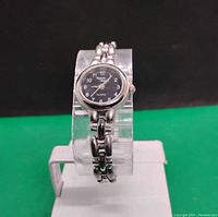 Front-facing photo of women's wristwatch showing black dial, silver-tone metal link bracelet, and watch face design.