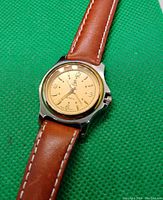 Close-up photo of the watch face and brown leather strap showing gold-tone dial and details.