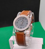 Front view of the women's quartz watch showing round white dial with black Roman numerals and brown leather strap with white stitching.