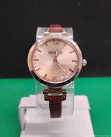 Front view of BREDA women's watch showing round rose gold case, analog dial with gold hour markers and brown leather strap.