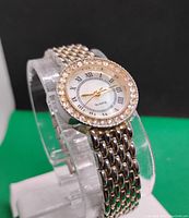 Front and side view of the women's quartz watch showing the crystal bezel, white dial with Roman numerals, and silver-tone metal link band.