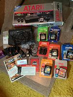 Photo shows the Atari 2600 console, two joystick controllers, 8 game cartridges in original boxes, some manuals, and documentation.
