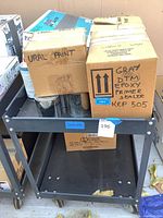 Metal cart loaded with cardboard boxes holding various automotive paints and parts, showing labels like Ural paint and Gray DTM Epoxy Primer Sealer.