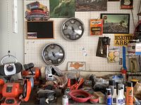 Overview of pegboard with two Chevy hubcaps, vintage-style garage signs, assorted garage products and tools below on bench including extension cords, sprays, and hardware.