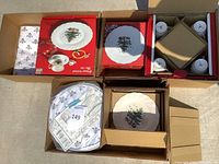 Photo showing six boxes containing Christmas themed plates and cups. Two plates and one set of four cups can be partially seen. Items are in original packaging and appear unused.