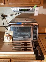 Photo of Farberware toaster oven with white timer and four knives in foam holder below it, plus Jwin radio mounted above.
