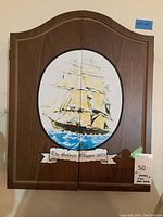 Wooden dart board cabinet with painted ship titled 'The Golden Clipper 1805'