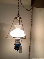 Photo of vintage hanging oil lamp lit and suspended by chain from ceiling showing frosted glass shade and metal detailing.