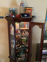 Full view of wooden glass display cabinet holding Harley Davidson collectibles and decor items on shelves.