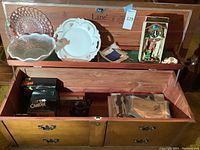 Wide view of the open Lane wooden chest showing all contents including plates, glass bowls, miniature cuckoo clock, lace napkins, candle box, tea kettle, and cutlery set.