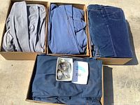 Three folded men’s coveralls in light grey, blue and navy alongside a small tray with three wristwatches