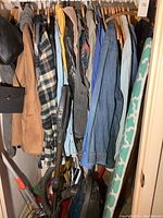 Photo of hanging men's coats and jackets in large and 2XL sizes, plus jean shirts on wooden hangers next to ironing board and cleaning supplies below