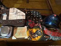 View of the lot including Bongo bag, Harley Davidson bandanas, blue motorcycle helmet with 'Ride' text and floral pattern, Sony Walkman CD player, framed art and folded Harley Davidson items.