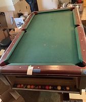 Full tabletop view showing green playing surface, wooden rails, one pocket corner, and built-in ball storage shelf with balls.