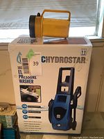 Yellow handheld flashlight placed on top of the original box for the Pacific Hydrostar 1650 PSI electric pressure washer.