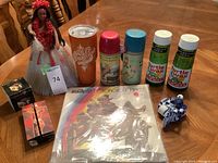 Photo of assorted collectibles including Roy Rogers thermos, Turtle Wax containers, Harley Davidson cup, motorcycle mama vinyl poster, and figurines on wooden table.