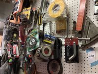 Wide view of pegboard with assorted tools, measuring tapes, packaged abrasives, and magnetic angle finder mounted.