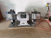 Front view of vintage dual bench grinder with two wheels, metal protective shields, mounted on metal base.