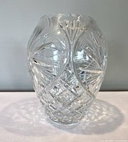 Clear cut crystal vase with intricate pinwheel and diamond cut patterns, standing on a flat surface.