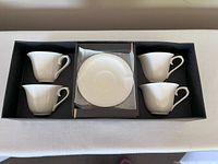 Four white ceramic tea cups and four matching saucers arranged in original black box.