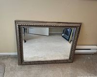 Full view of the rectangular mirror with ornate gold frame leaning against a wall on carpeted floor.