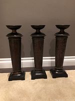 Three Pier 1 candle holders standing side by side against a grey wall, showing overall design and size.