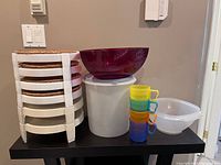 Full view of the lot showing six white pie stackers, large white container with blue lid, red triangular salad bowl, white mixing bowl, and four colorful cups.