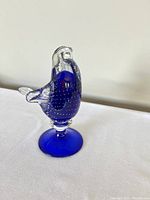 Front view of the cobalt blue Murano art glass bird figurine showing clear glass head and wings, perched on a blue circular base.