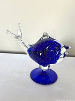 Clear view of the fish figurine standing on a solid cobalt blue base, showing the overall shape and color.