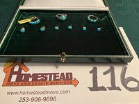 Photo showing three rings placed in a green velvet jewelry display box with three pairs of turquoise pierced stud earrings, all on a green velvet background.