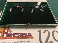 Top view photo showing both sets of rings and matching earrings inside a green jewelry box with black velvet base.