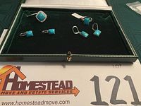 Photo shows a box with one square turquoise ring, one pair of square turquoise earrings and one pair of rectangular turquoise earrings, all set in silver.