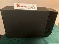 Front view of black Bose speaker unit with control knobs and Bose logo, placed on green tablecloth.