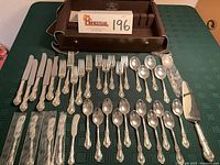 Full layout of 37 sterling flatware pieces arranged in front of Gorham chest on green tablecloth