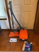 Kenmore canister vacuum cleaner and detachable hose with upright handle, shown with box of extra vacuum bags beside it on wooden floor.