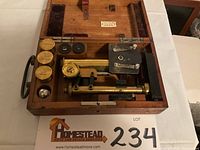 Top view of the Leitz Wetzlar microscope in an open wooden case with accessories including three brass lens containers and two smaller lenses.