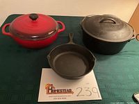 Front view of all three cookware pieces: red enamel covered Dutch oven, black cast iron skillet, and black cast iron covered Dutch oven