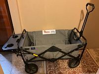 Full view of Mac Sports folding wagon showing foldout side beverage tray with cup holders, gray fabric body, black metal frame and handle extended.