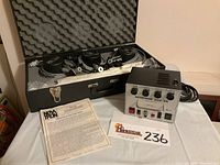 Voltage regulator unit alongside the foam-lined carrying case storing three flash heads and cables, with instruction sheet visible.