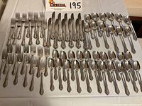 Flatware set displayed showing full count of knives, forks, tablespoons, salad forks, and teaspoons laid in rows on white cloth surface.