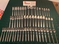 Full set of mid-century modern flatware laid out on green cloth, showing all knives, forks, spoons, and serving pieces in neat rows.