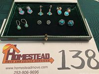Photo showing six pairs of pierced earrings in a green velvet box, featuring turquoise and gemstone set silver earrings.
