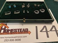 Full view of six pairs of earrings in green velvet box, showing variety of styles and stones.