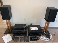 Wide front view showing speakers on stands flanking stereo components, remotes and cables laid out