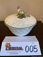 Front view of cream-colored woven pattern bowl with green band and colorful bird handle on lid.