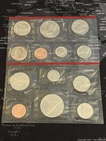 Two unopened proof-like coin sets sealed in plastic packaging. Each set contains multiple coins including half dollars and smaller denominations.