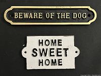 Front view of both cast iron signs showing the text "BEWARE OF THE DOG" and "HOME SWEET HOME"
