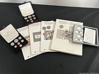 Overview of entire lot of coins and stamp collections showing 23 coins and multiple souvenir stamp collection booklets.